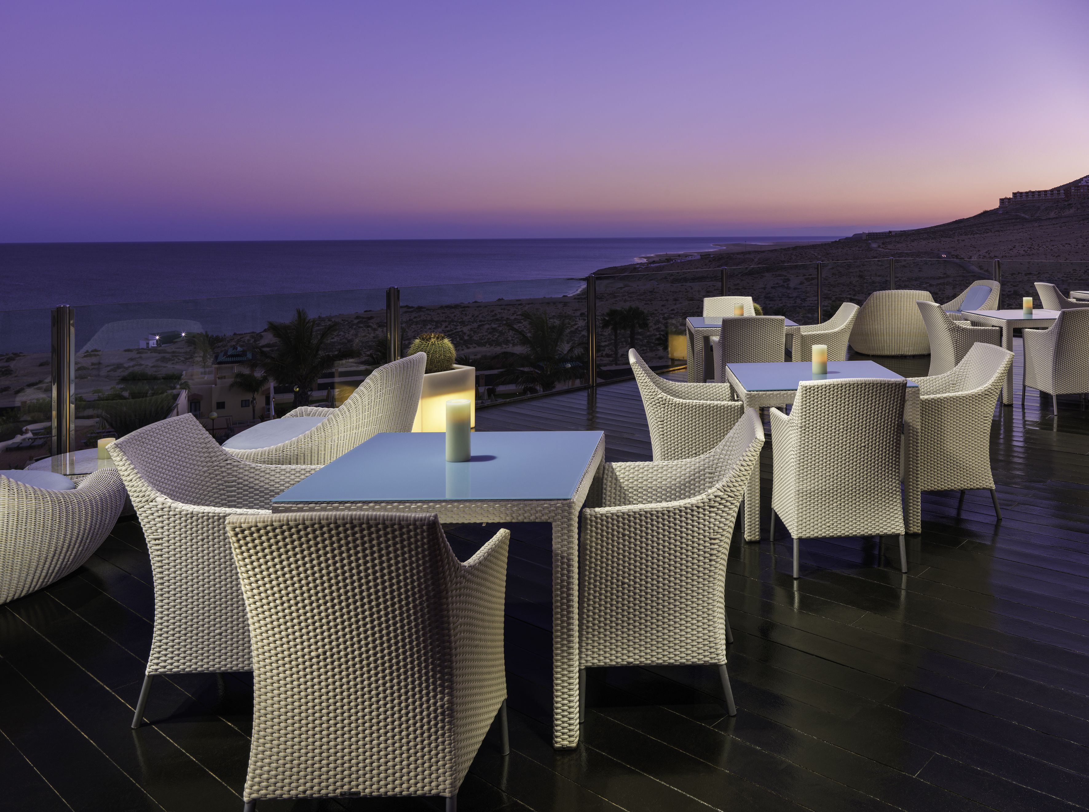Una terraza con mobiliario de mimbre y vista al mar al atardecer.