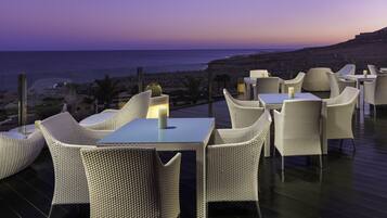 Una terraza con mobiliario de mimbre y vista al mar al atardecer.