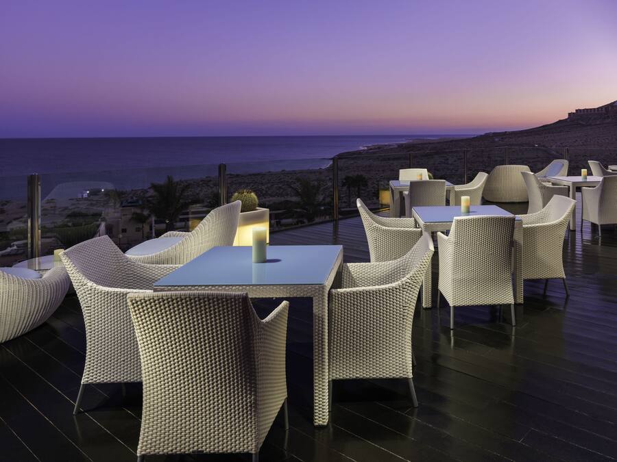 Una terraza con mobiliario de mimbre y vista al mar al atardecer.