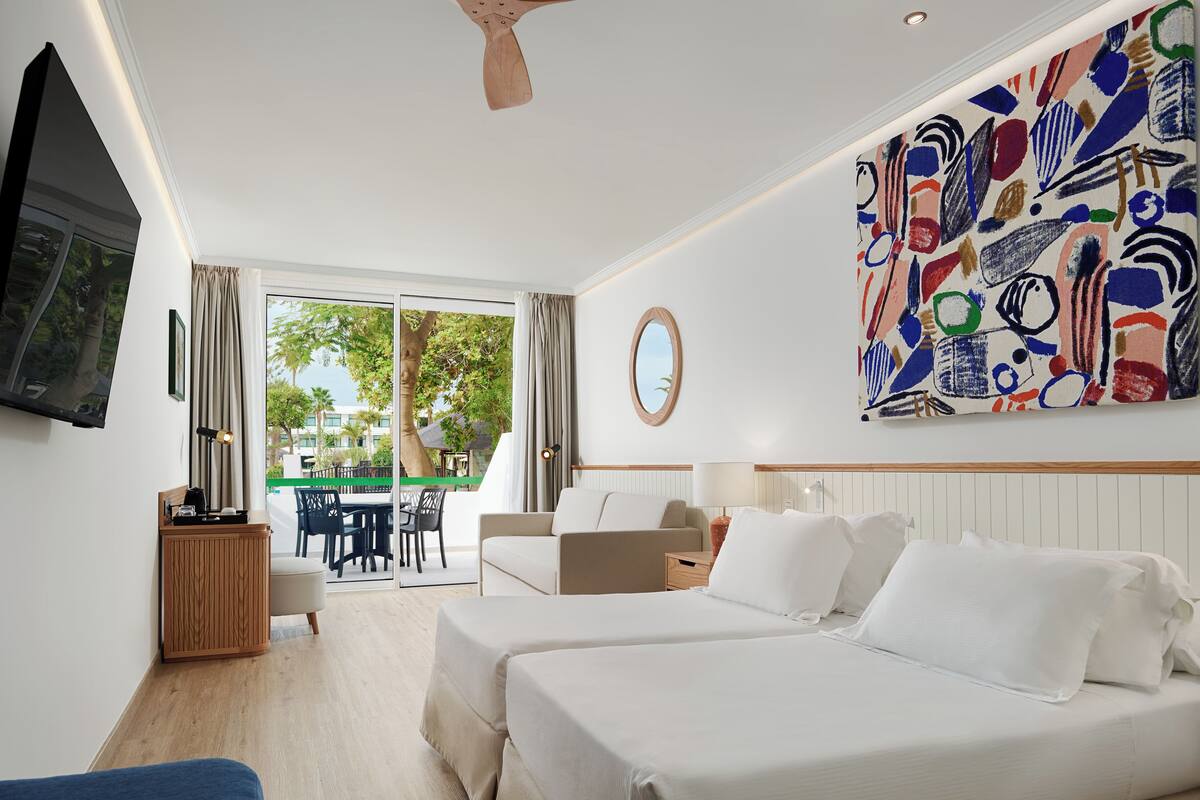 A hotel room with two beds, a TV, a desk, and a painting.