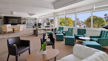 A spacious lounge area with a mix of seating options including sofas and chairs, a coffee table with a potted plant, and a view of the outdoors through large windows.