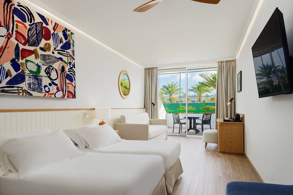 A hotel room with two beds, a balcony with a table and chairs, a TV, and a large abstract painting on the wall.