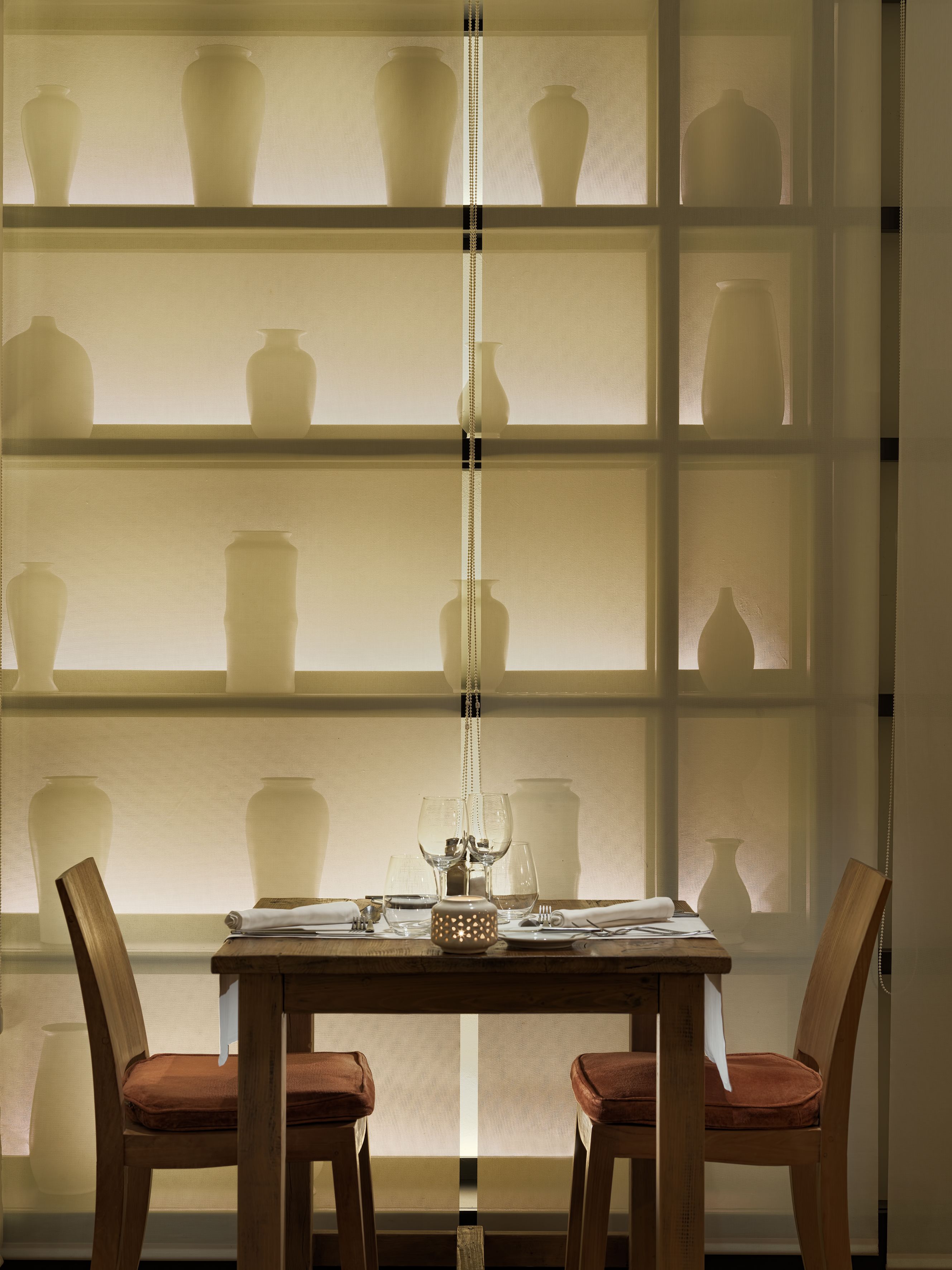 A dining table with chairs, a vase, and a bottle on the table.