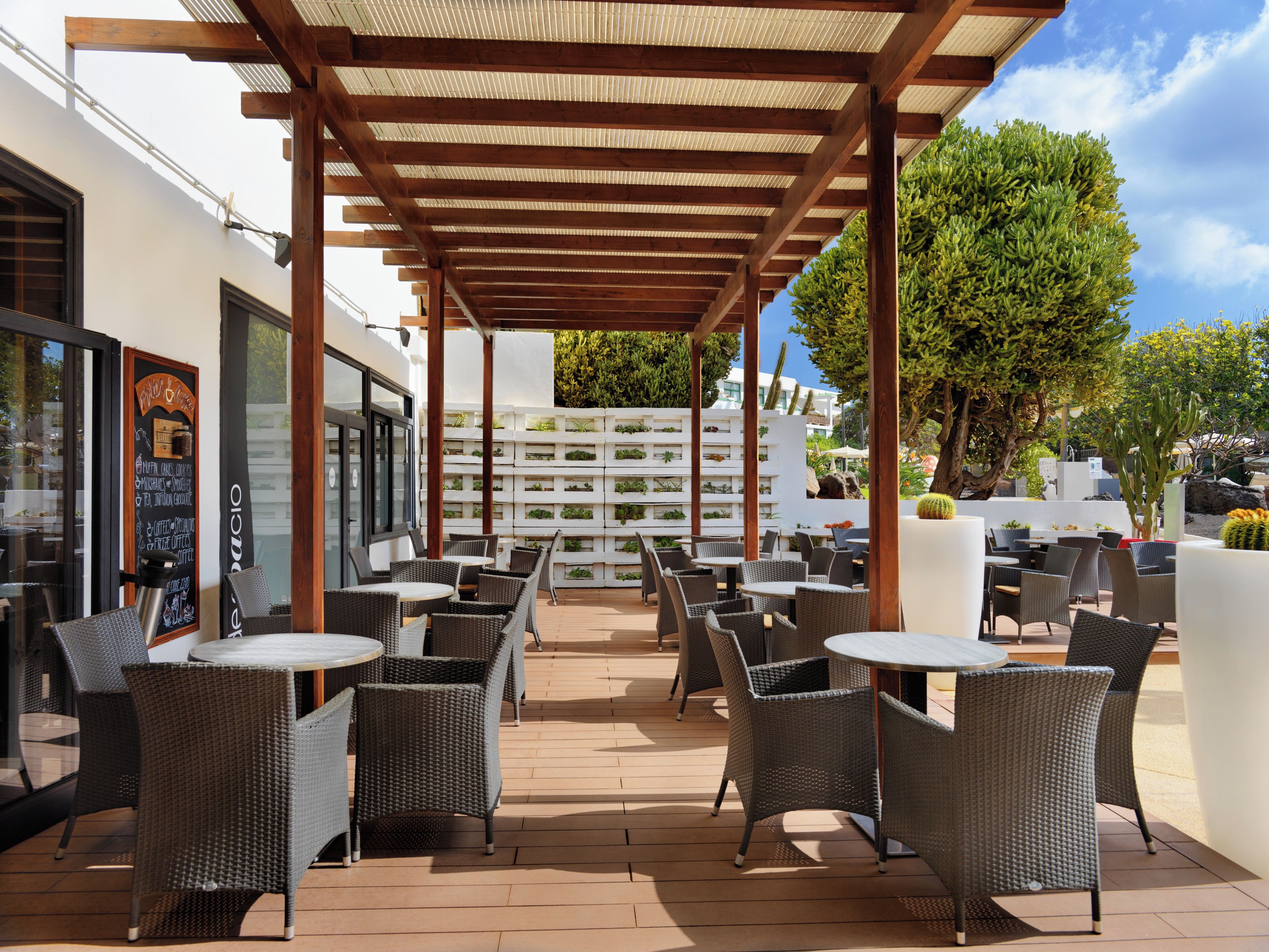 An outdoor patio with wicker furniture, a pergola, and a white wall with a menu board.