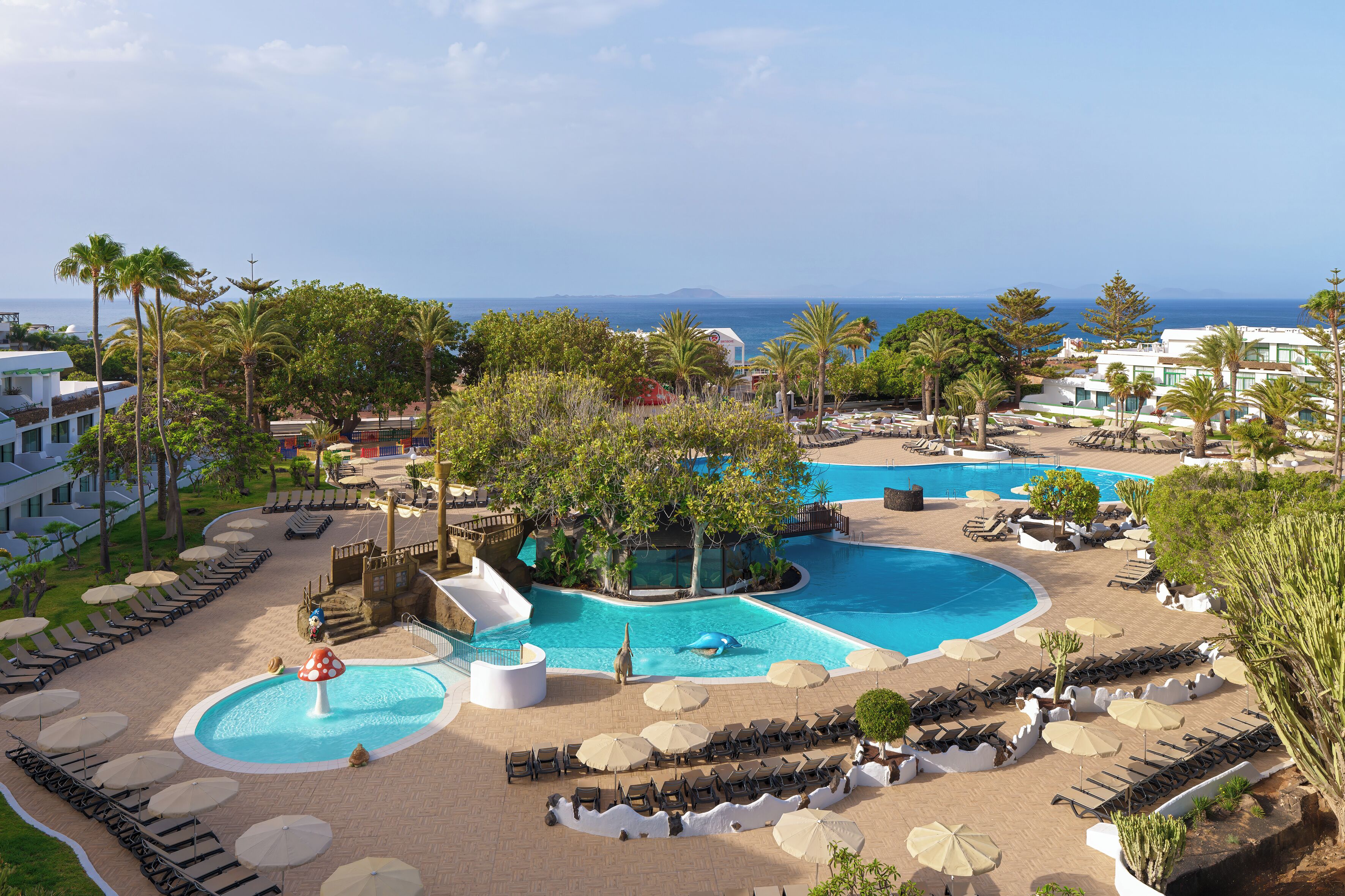 A resort with multiple swimming pools, palm trees, and a view of the sea.
