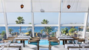 A restaurant with tables and chairs arranged near a pool, overlooking the ocean. - H10 Timanfaya Palace (Yaiza)