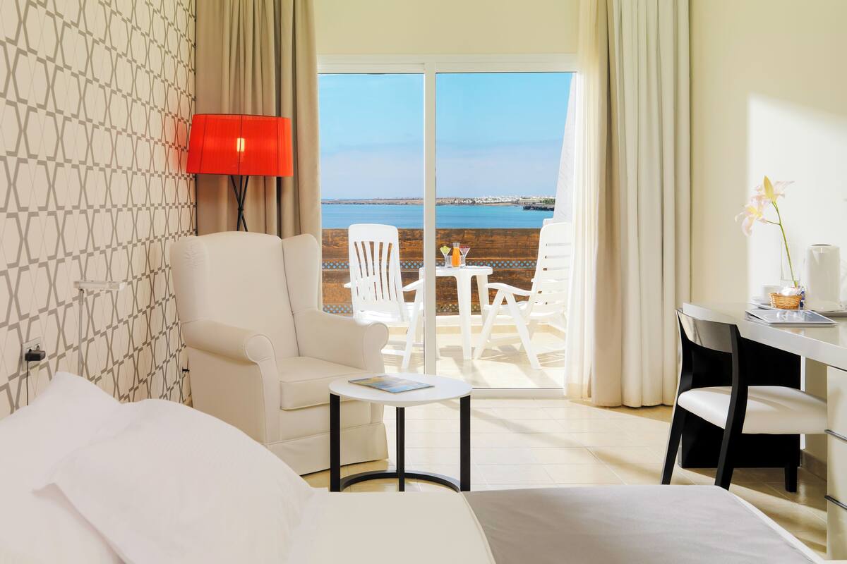 Una camera d'albergo con un letto, una scrivania, una sedia, un tavolo e vista sul mare.