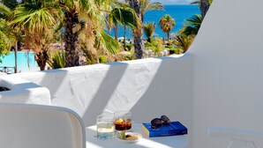 A white balcony with a table set for two, overlooking a beach with palm trees and the sea. - H10 Timanfaya Palace (Yaiza)