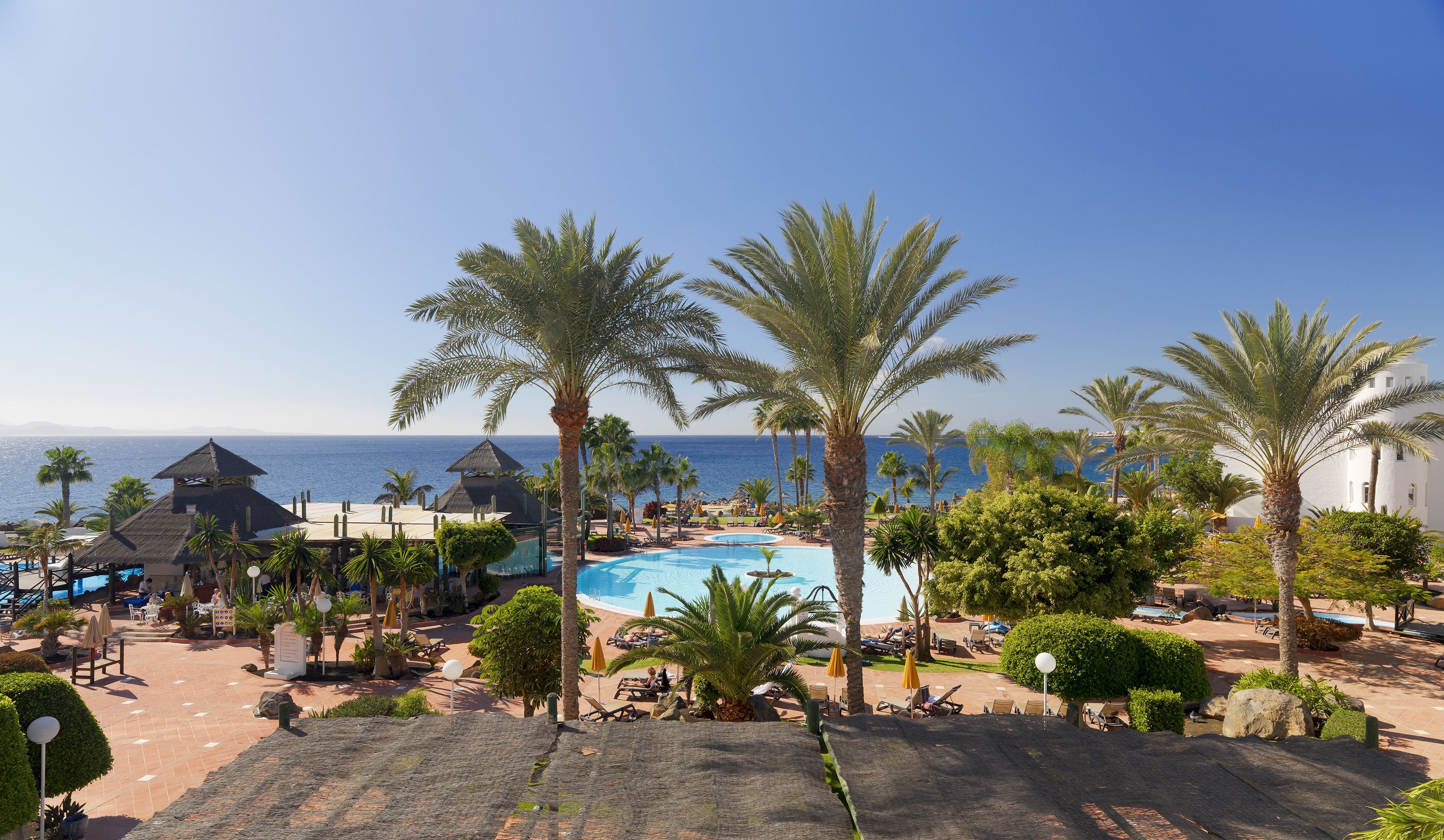 Een resort met een zwembad, palmbomen en uitzicht op zee.