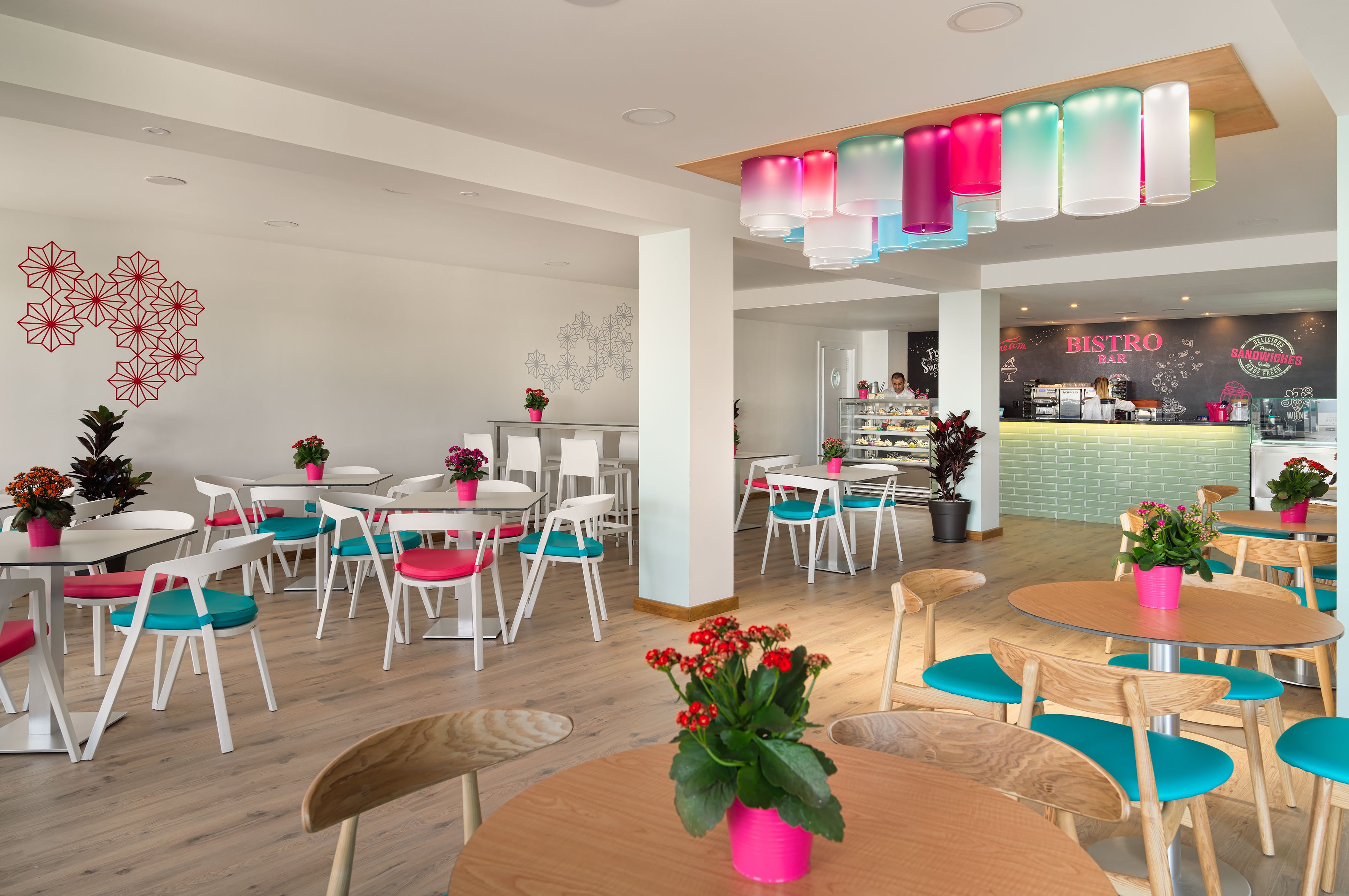 Um bistrô moderno com mesas e cadeiras redondas, um lustre colorido no teto e uma parede com a placa 'BISTRO'.