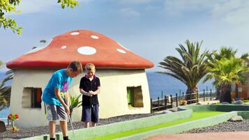 Two people playing golf near a mushroom-shaped building with a view of the ocean.