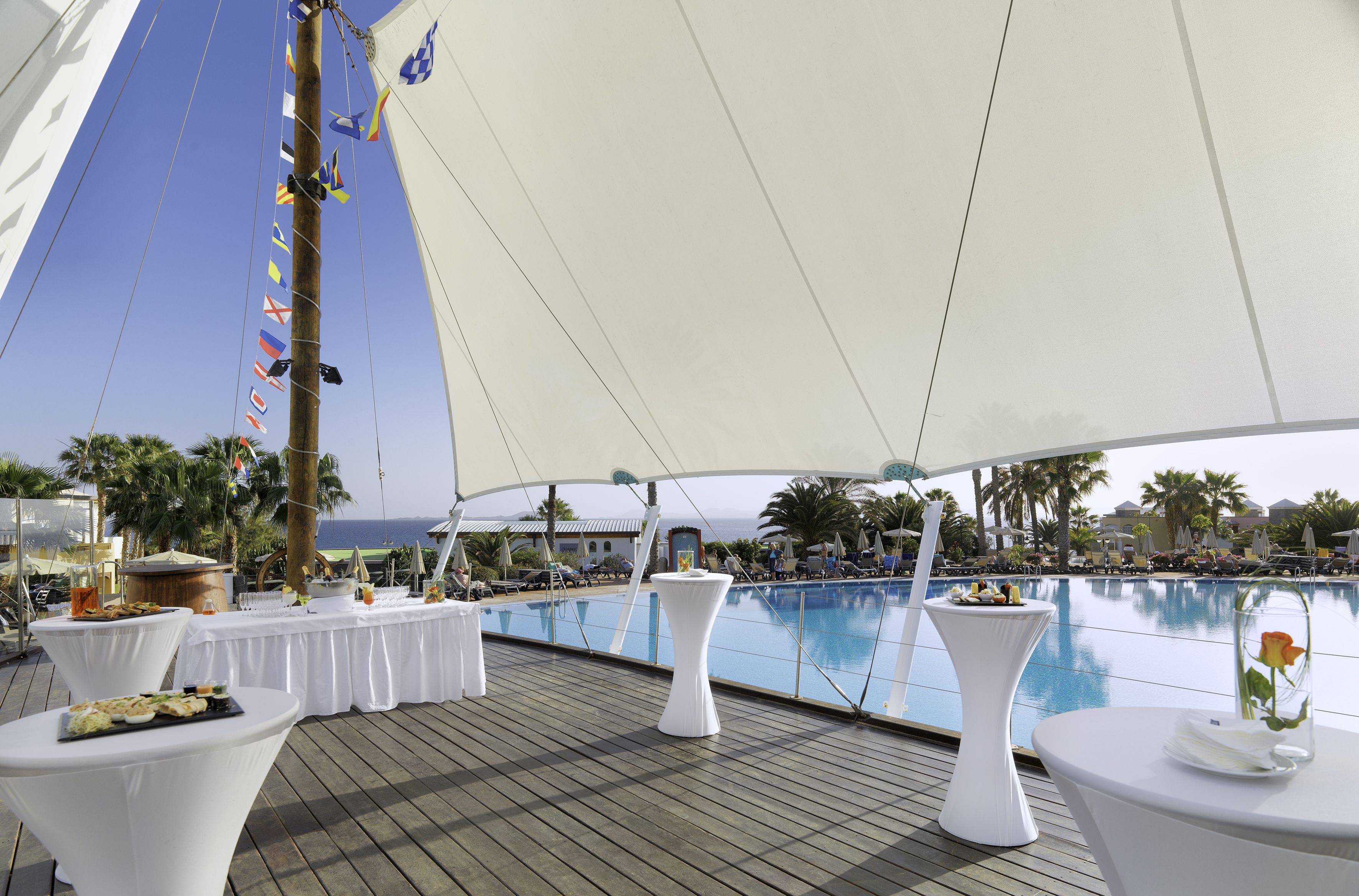 A deck with tables set for dining, overlooking a pool and a view of the ocean.