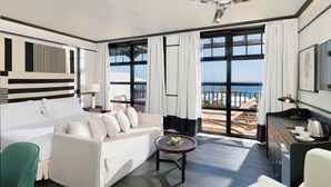 A modern hotel room with a bed, sofa, and a balcony with a view of the sea.