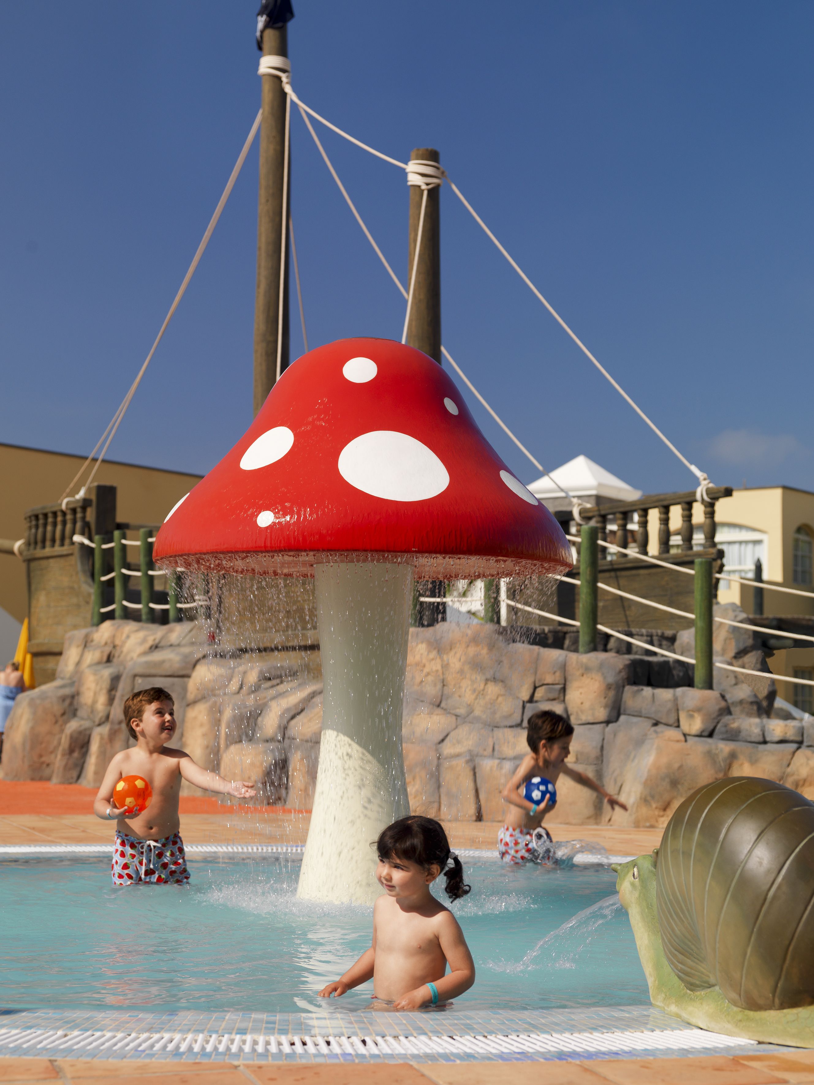 A water play area with a large mushroom-shaped water feature, a pool, and a rock wall.