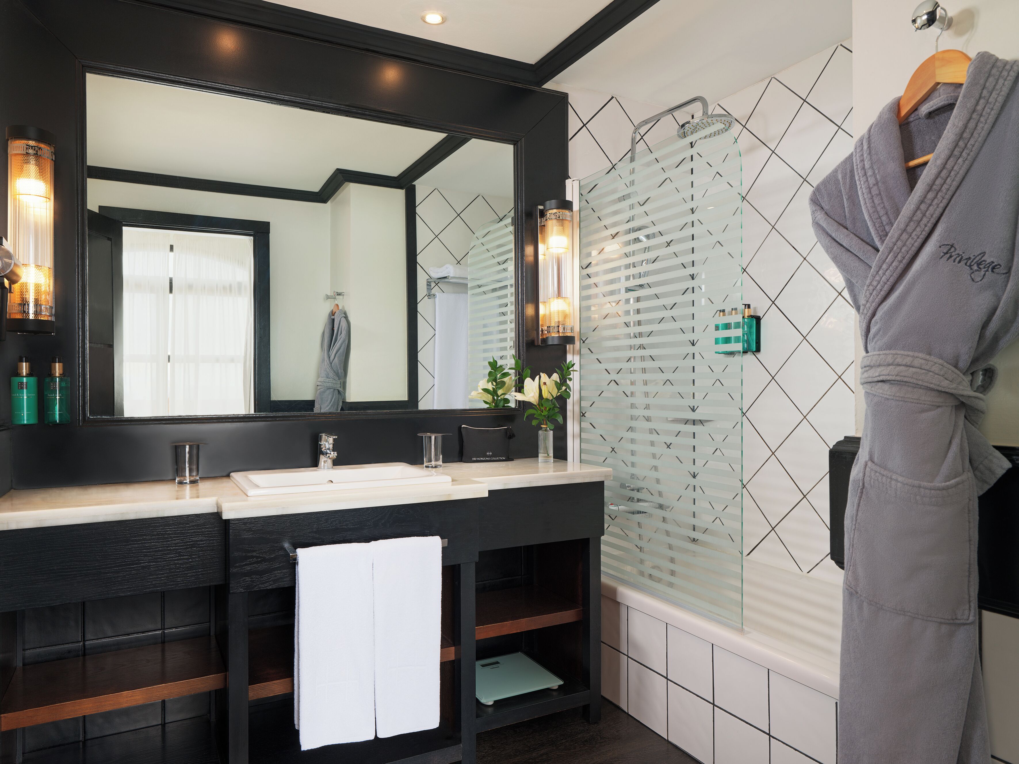 Un baño moderno con un espejo grande, lavamanos dobles, cabina de ducha de vidrio y una bata colgada en un perchero.