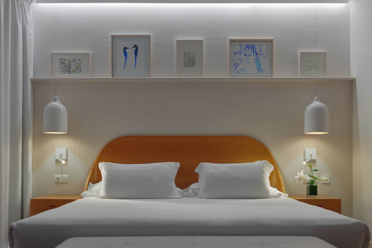 A neatly made bed with white linens, a wooden headboard, and wall-mounted picture frames.