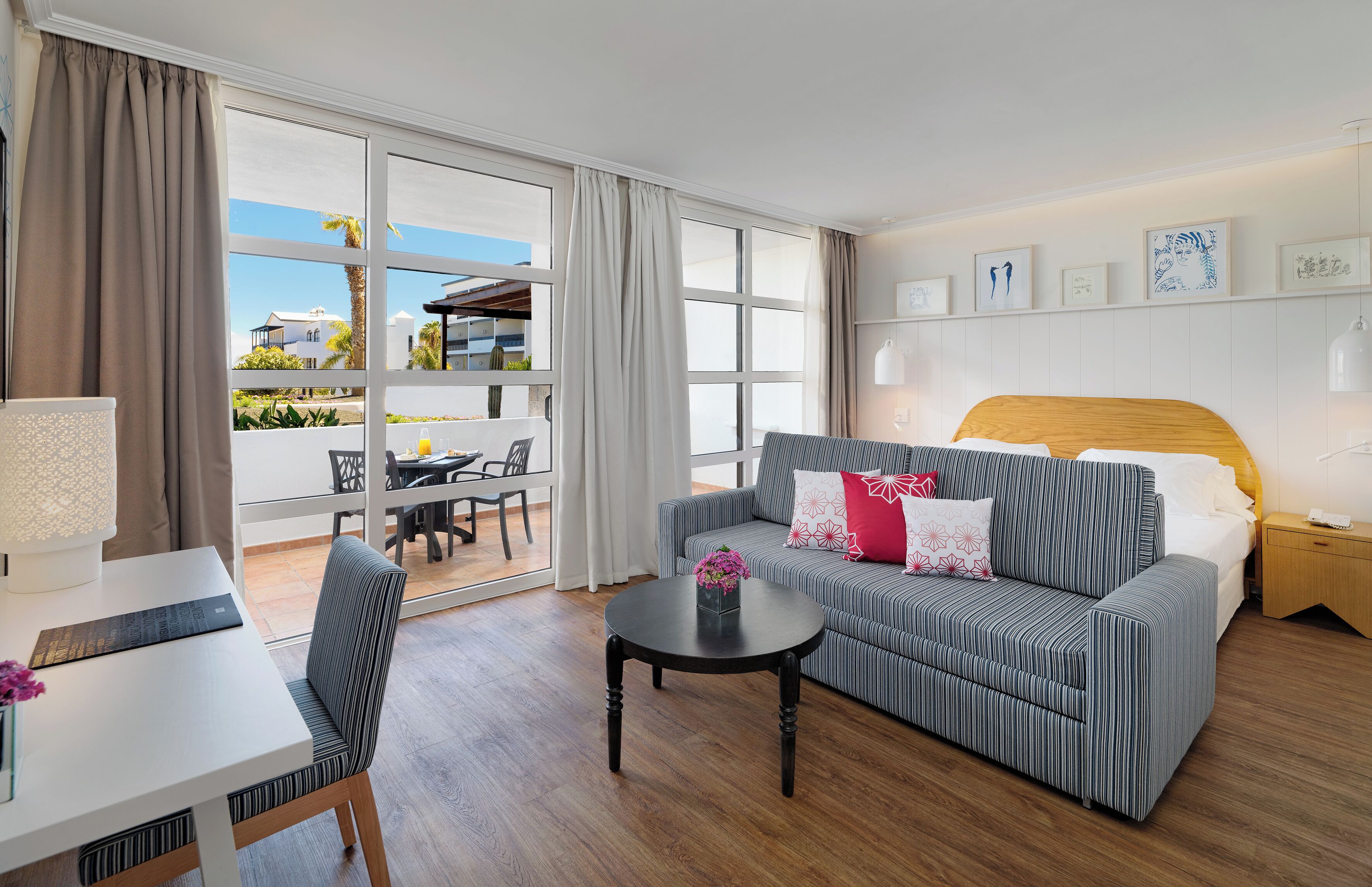 Habitación de hotel con un ventanal grande, un sofá, una cama, una mesa y una silla.