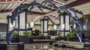A spacious lobby with modern furnishings, a high ceiling, and decorative dolphin sculptures.