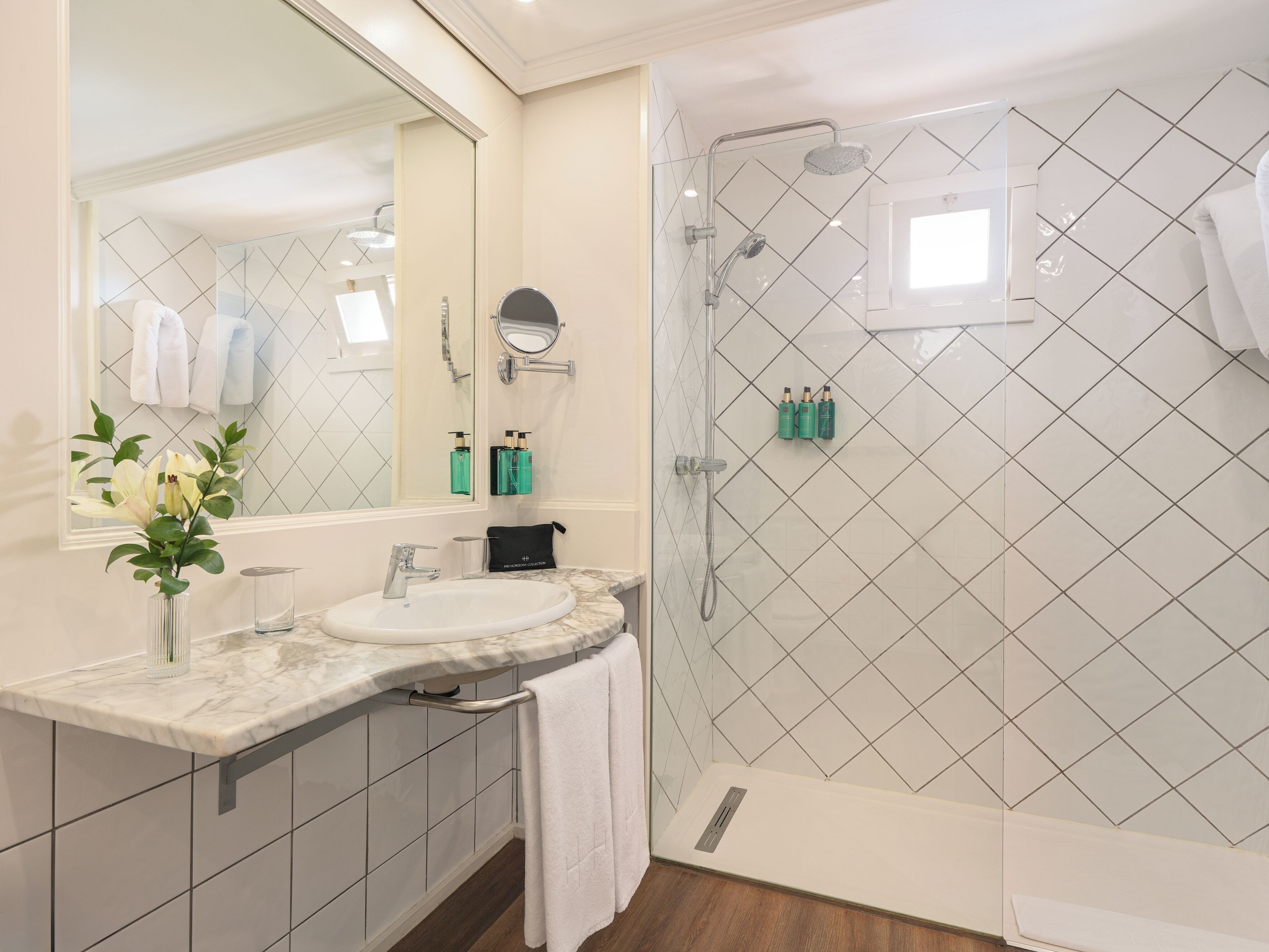 Un bagno moderno con un lavabo in marmo, cabina doccia in vetro e uno specchio grande.