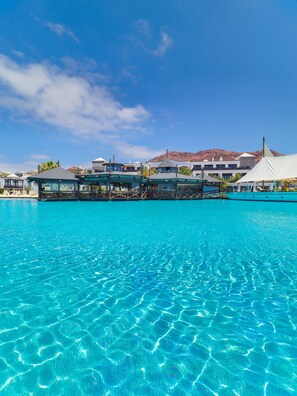 Una piscina azul cristalina con vistas a un edificio de resort y una montaña al fondo.