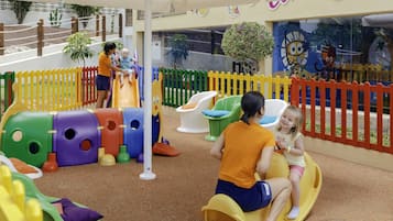 Un espacio de juegos infantiles con estructuras coloridas, un tobogán y zonas de estar.