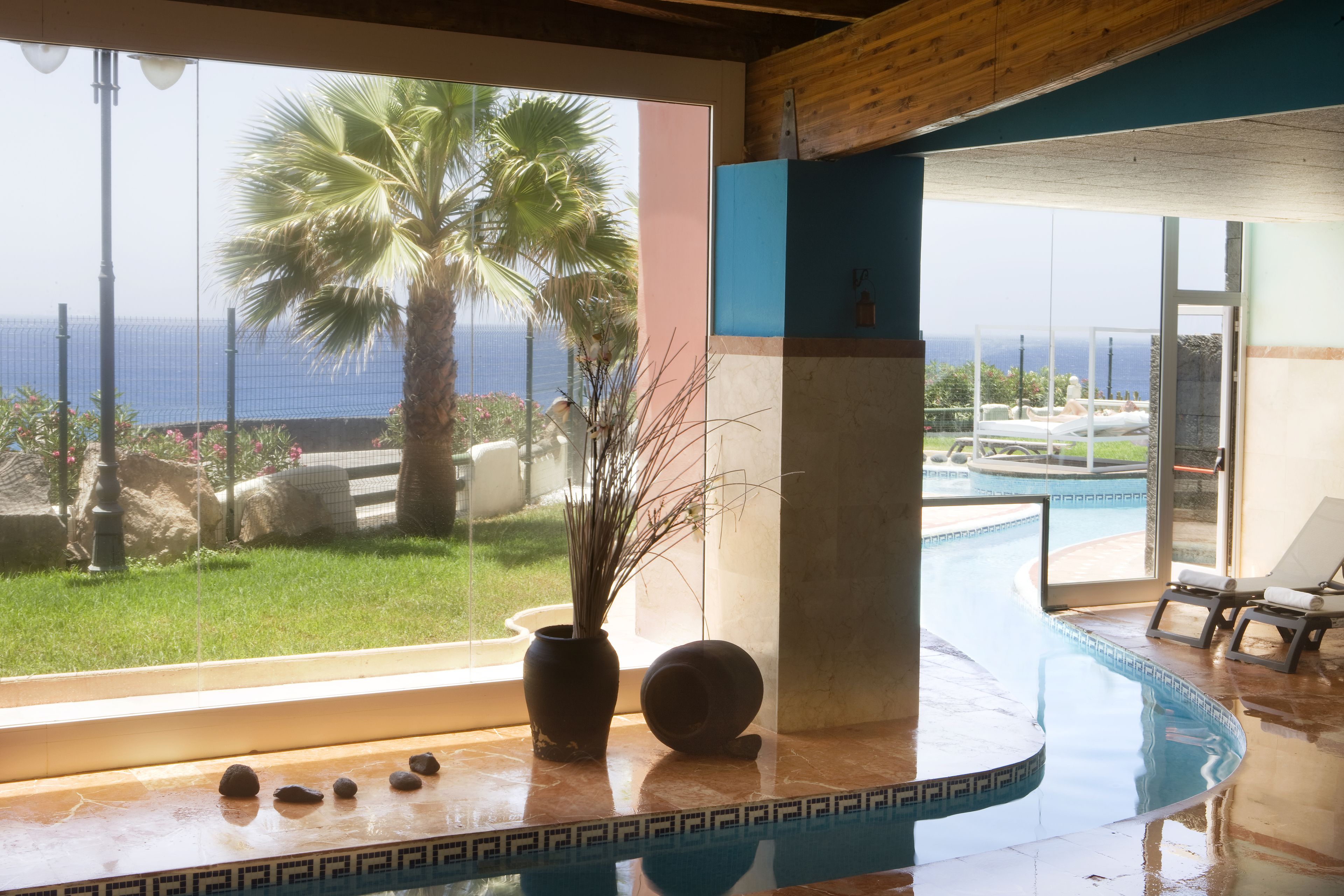 A pool area with a view of the ocean, a palm tree, and a lounge chair.