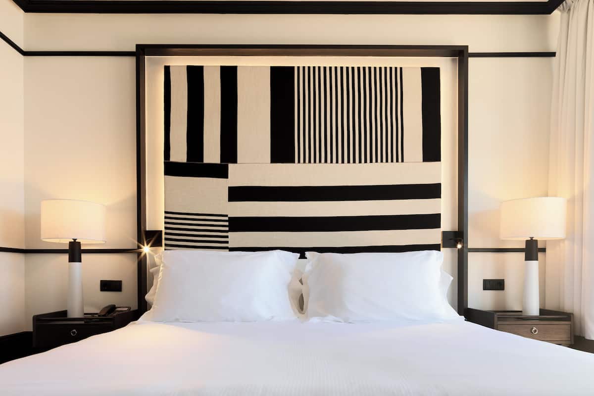 A hotel room with a large bed, two bedside tables, and a modern headboard with geometric patterns.