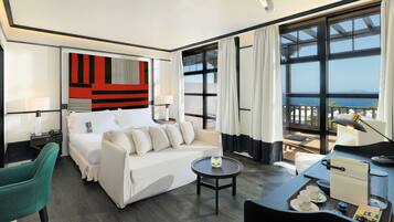 Habitación de hotel con cama, sofá, mesa de centro, escritorio y vistas al mar.