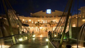 Un pont menant à un hôtel reconnaissable à son enseigne bien visible, à ses palmiers et à son entrée bien éclairée.