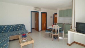 A living room with a sofa, a coffee table, and a dining area with chairs and a table. There is a kitchen area with cabinets and a television. - HL Paradise Island (Yaiza)
