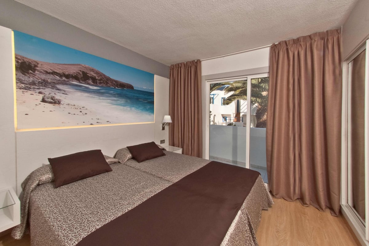 Ein Hotelzimmer mit einem großen Bett, einem Wandgemälde mit Strandmotiv und einer Schiebetür nach draußen.