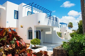 Un edificio blanco con detalles azules, un pequeño árbol y un muro de piedra.