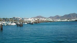 A marina with boats docked, a clear blue sky, and buildings in the background. - HL Paradise Island (Yaiza)