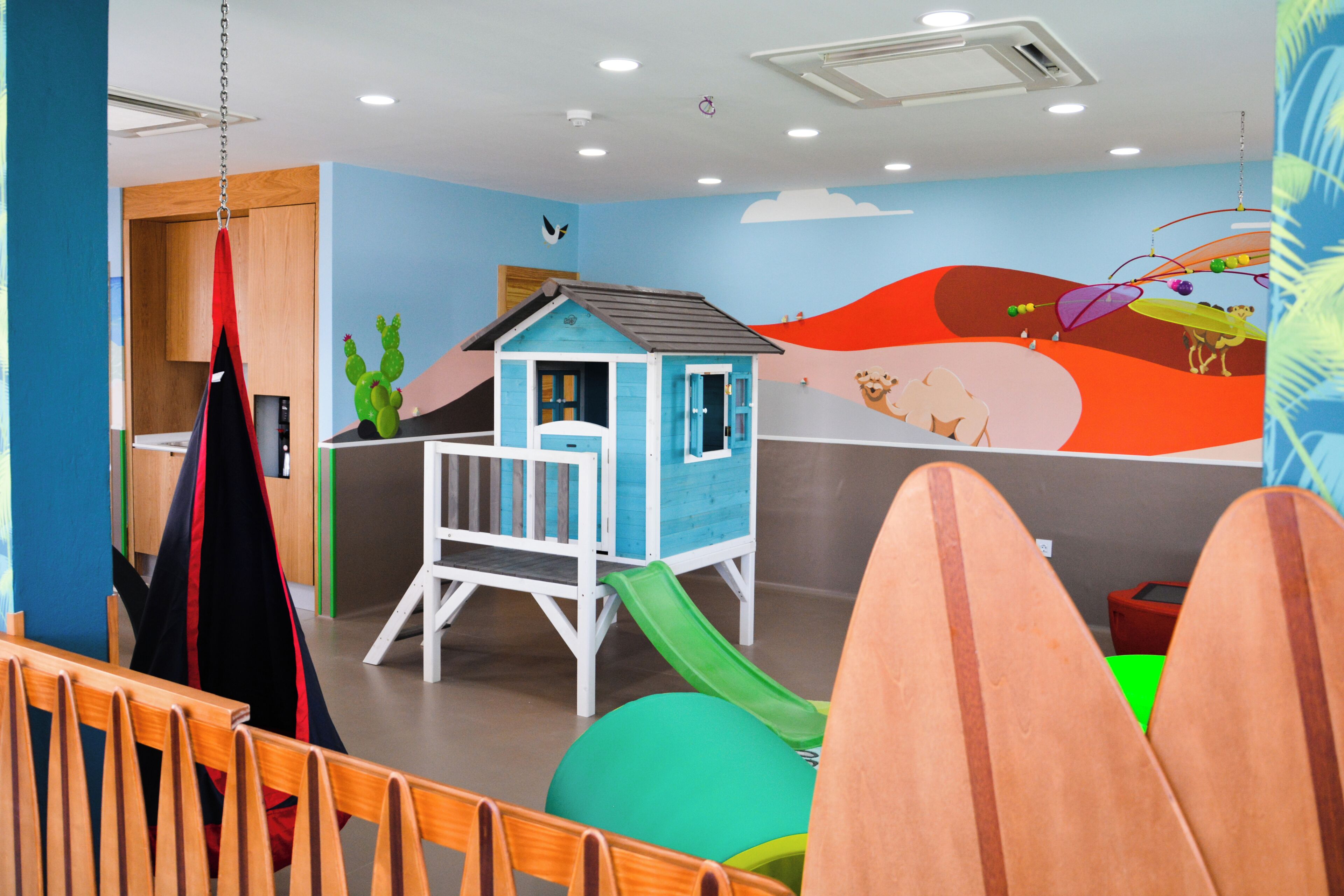 Un'area giochi per bambini con una piccola casetta blu, uno scivolo e decorazioni colorate.
