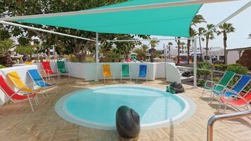 Zona junto a la piscina con piscina, sillas de descanso y una pérgola sombreada.