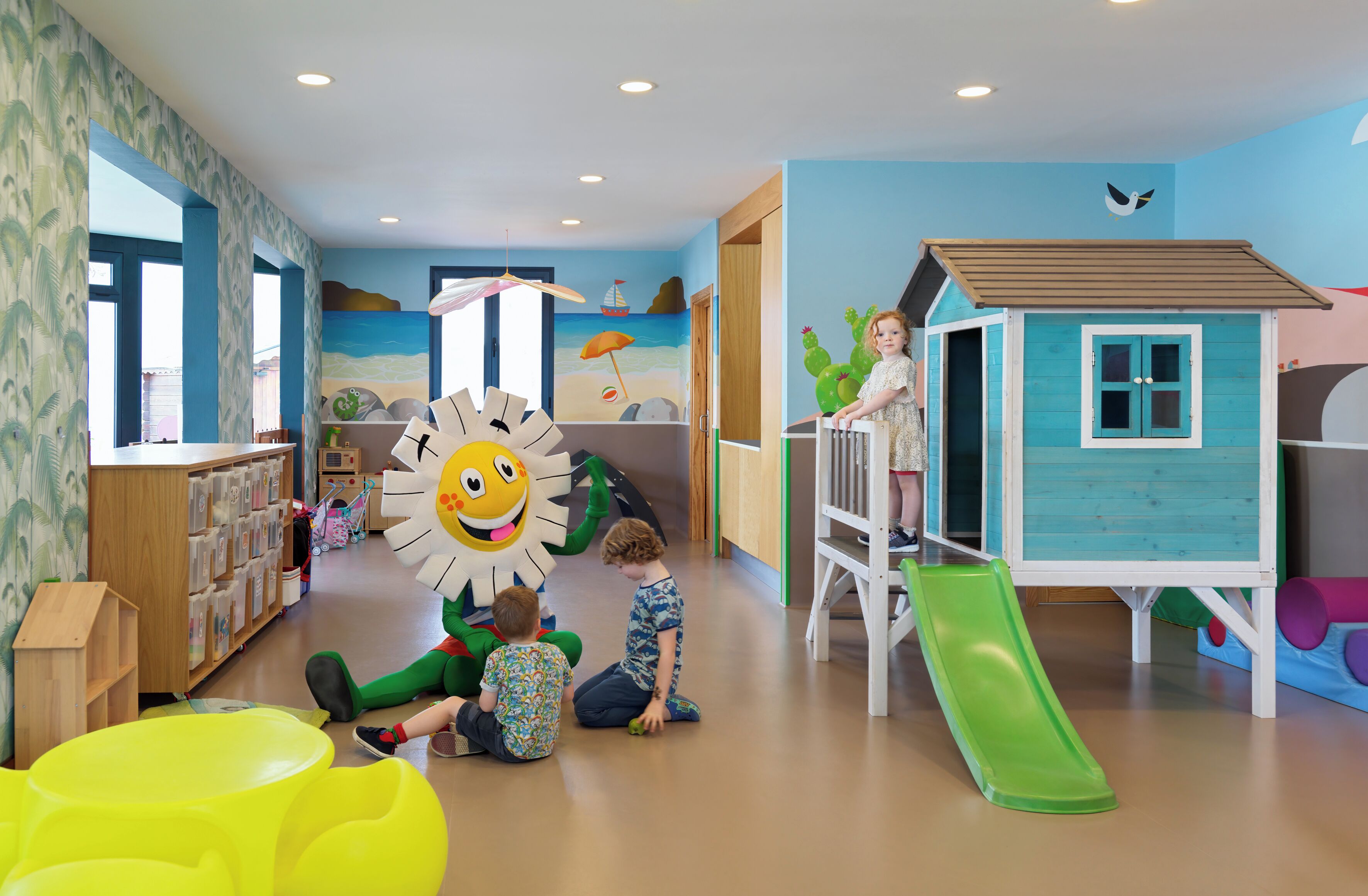 Zona infantil con un tobogán, una casita de juegos y una gran decoración de sol.