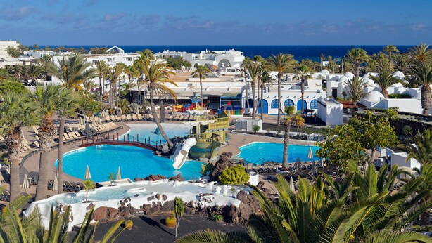 Un resort con varias piscinas, palmeras y vista al océano.
