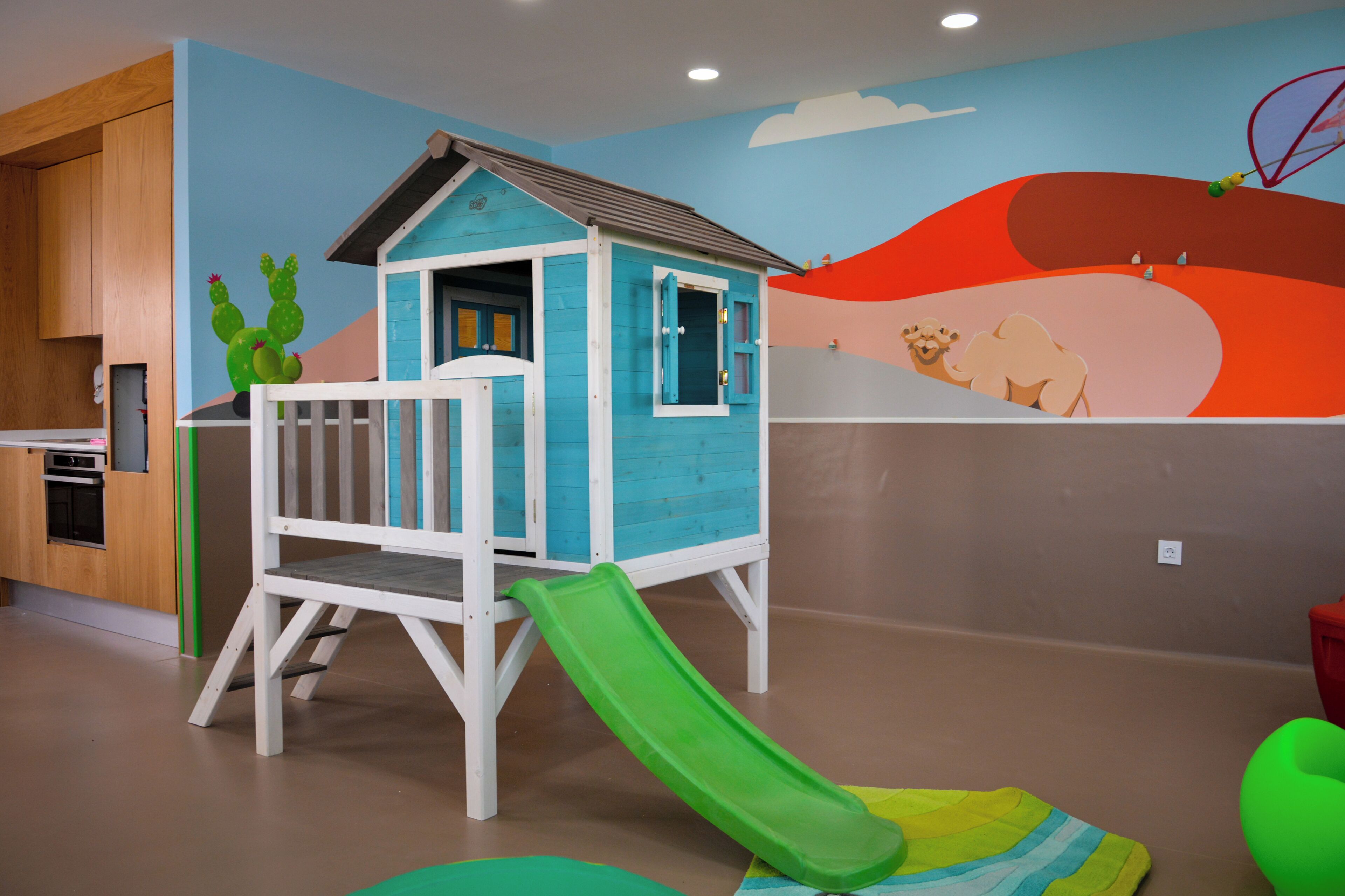 Un espace de jeux pour enfants avec un toboggan, une cabane et une fresque murale.