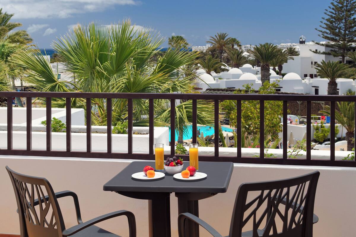 Un balcon avec une table dressée pour deux personnes, deux chaises et une vue sur une piscine et des bâtiments.