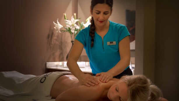 Sesión de masoterapia en un spa, con un cliente recostado en una camilla y un terapeuta atendiendo.