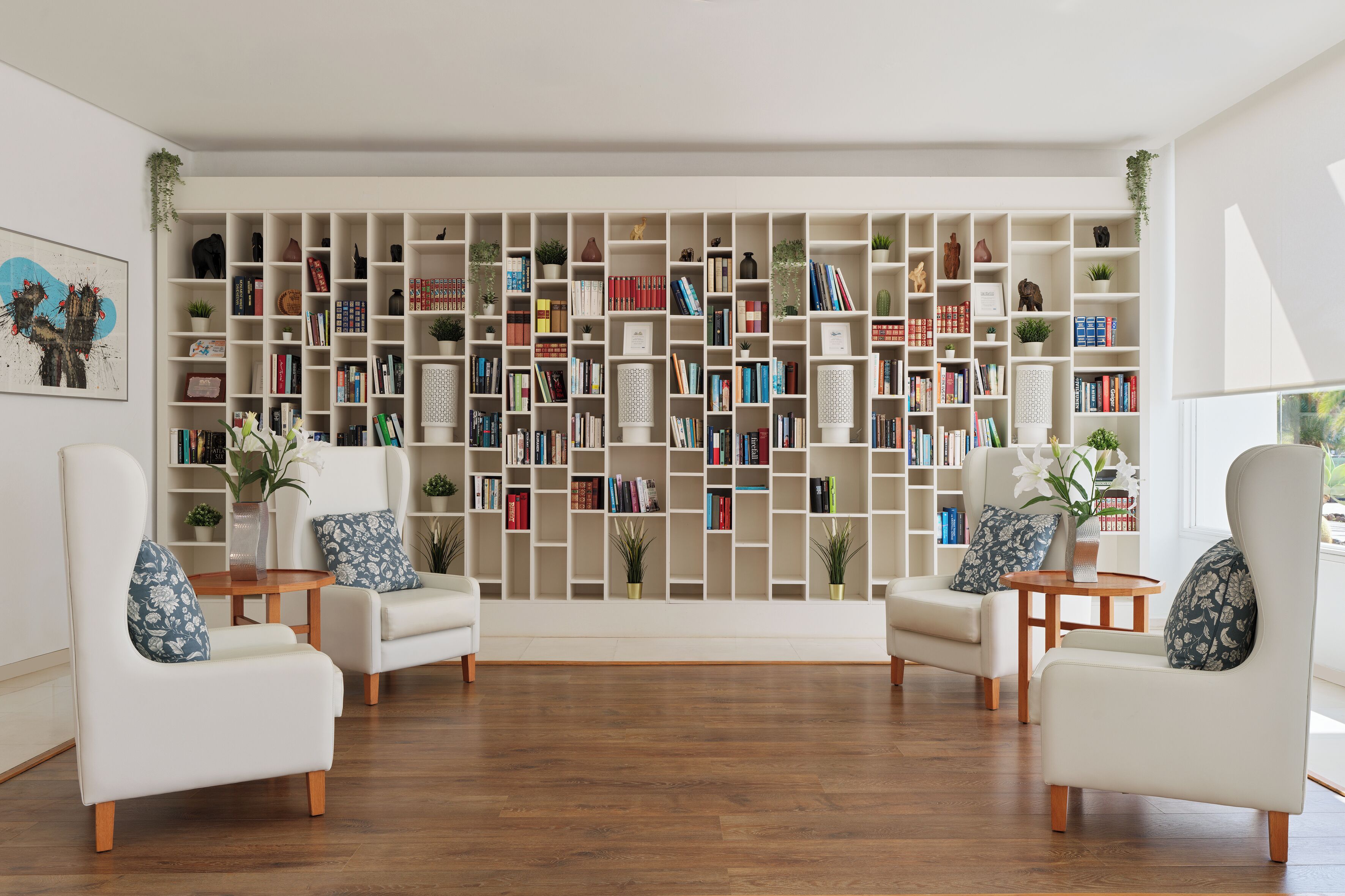 Una sala de estar moderna con una gran estantería, dos sillones blancos, una mesita y un jarrón con flores.