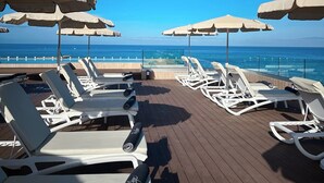 Terraza con sillones blancos y sombrillas color beige, con vistas al mar azul y transparente.