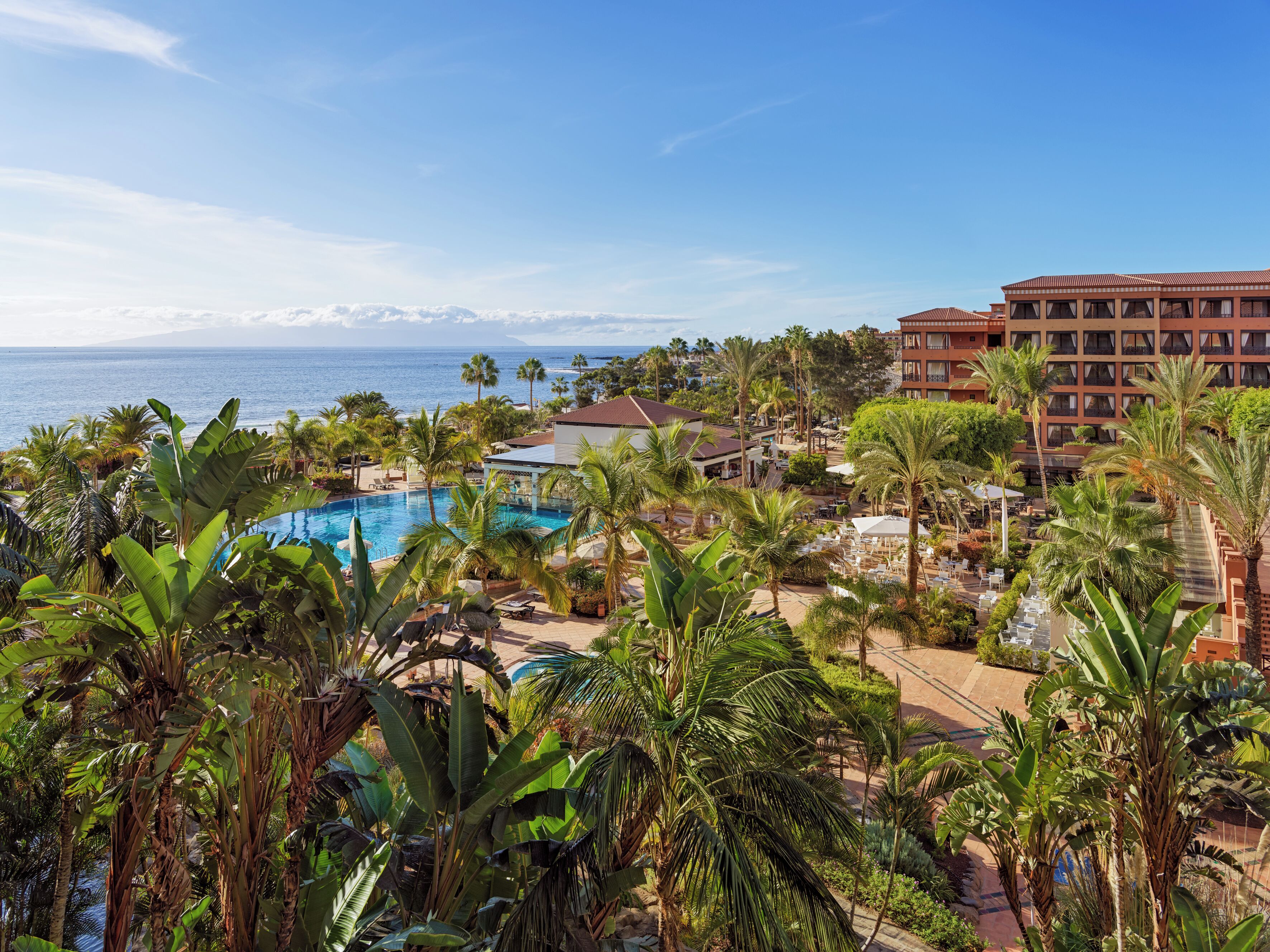 Um resort com piscina, palmeiras e vista para o oceano.