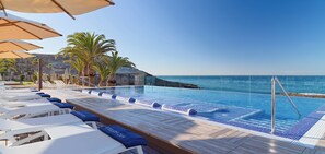 A poolside area with lounge chairs and umbrellas, a clear view of the ocean, and a rocky landscape in the background. - H10 Costa Adeje Palace (Adeje)