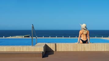 Un espace piscine doté d’une terrasse en bois, d’un escalier métallique pour accéder à la piscine et offrant une vue sur l’océan.