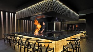 Zona de bar moderna con una isla central, taburetes y un chef realizando un espectáculo de fuego.