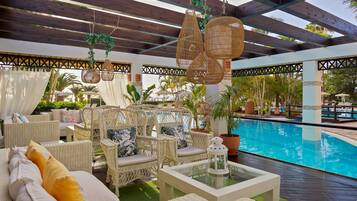 A poolside area with wicker furniture, hanging wicker lamps, and a glass table.