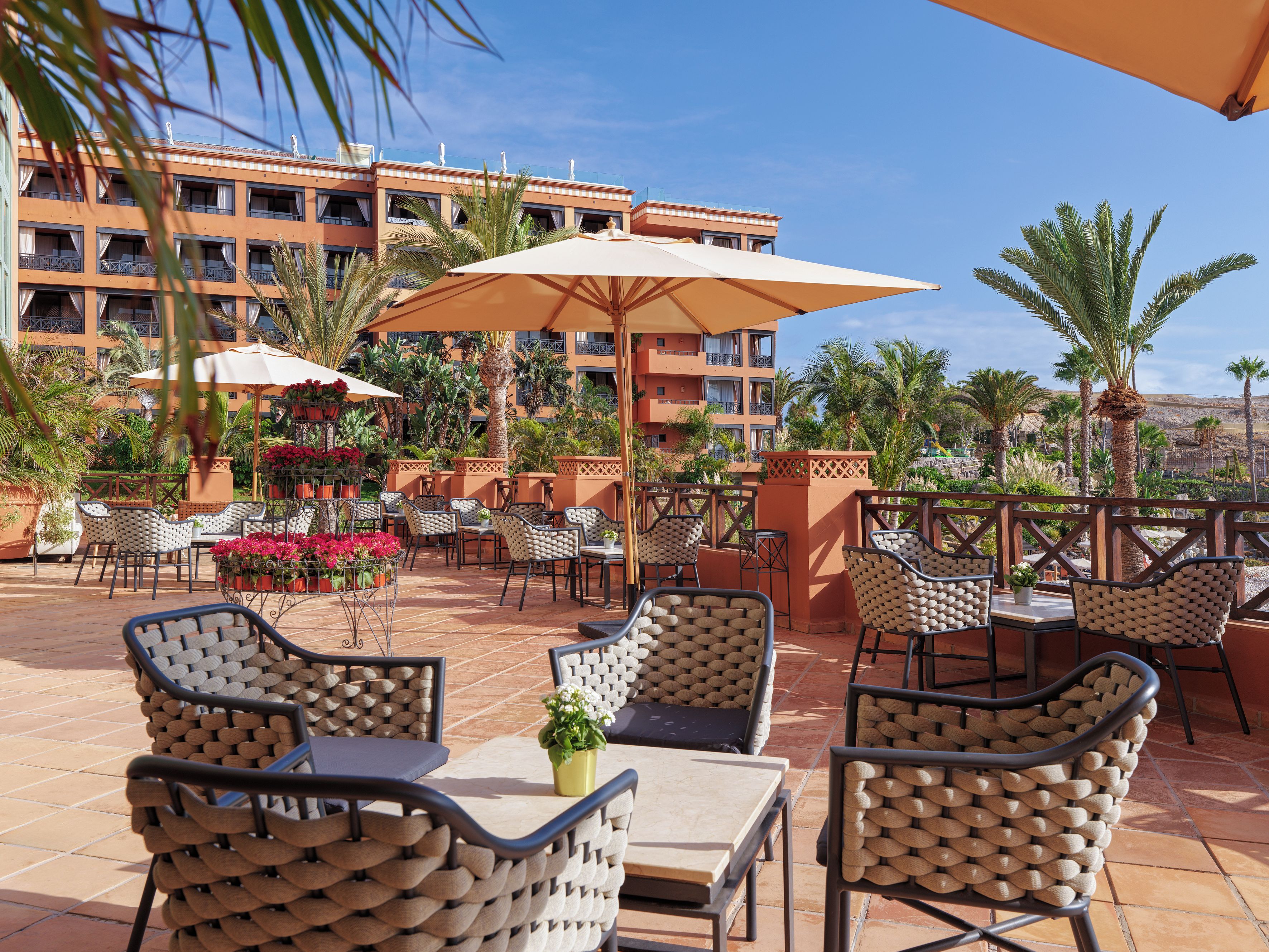 An outdoor patio with wicker furniture, umbrellas, and potted plants.