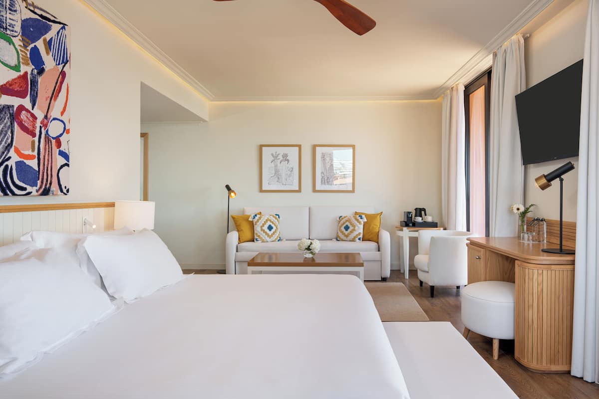 A hotel room with a large bed, a sofa, a desk, and a TV.