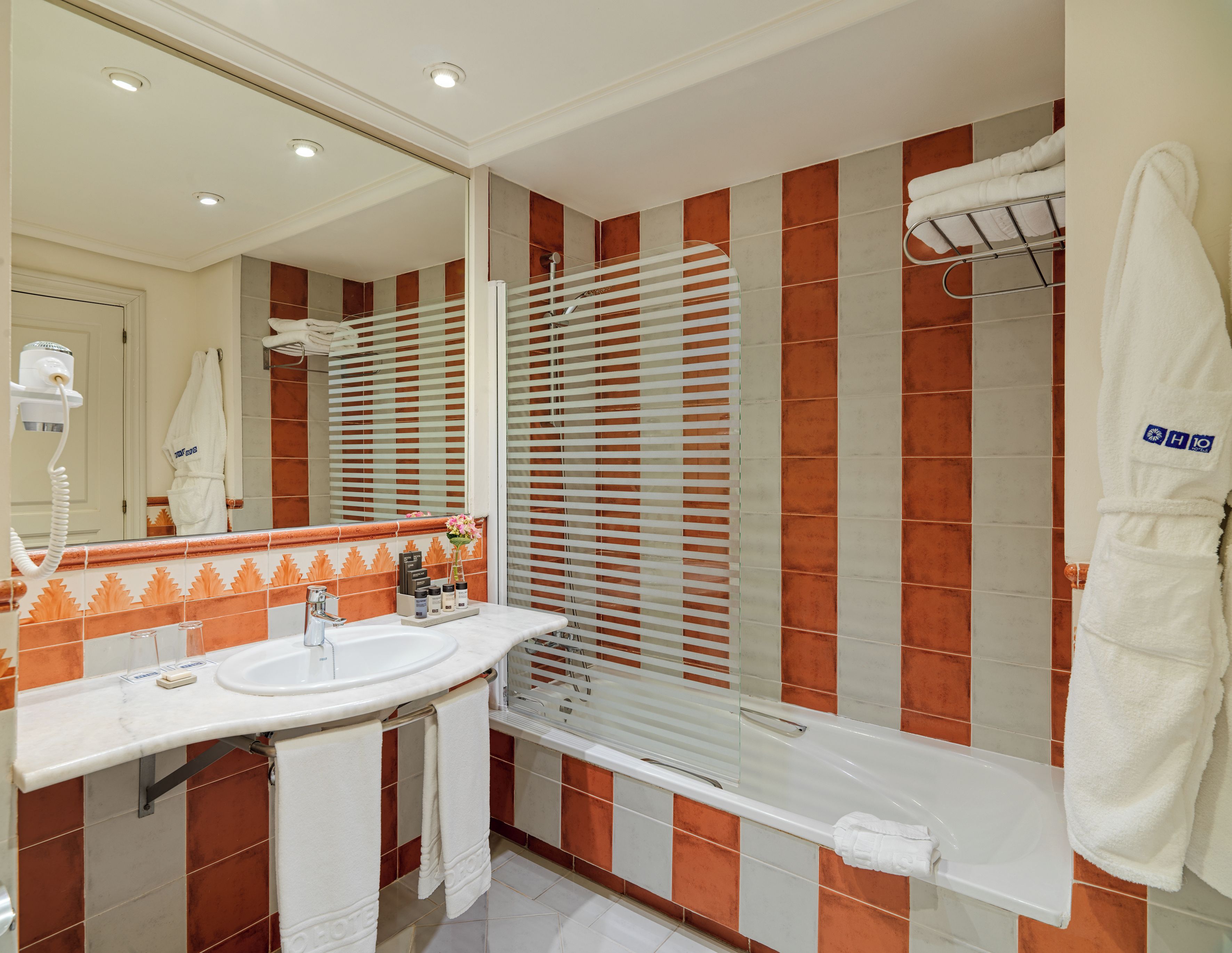 A bathroom with a sink, mirror, shower, and a towel rack.